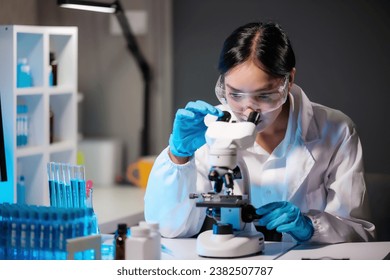 Asian female scientist looking under microscope, analyzes petri dish sample. specialists working on medicine, biotechnology research in advanced pharmacy lab, Medical development laboratory.