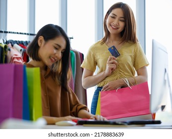 Asian Female Seller Smiling And Putting Garment In Paper Bag For Happy Woman With Credit Card In Shop