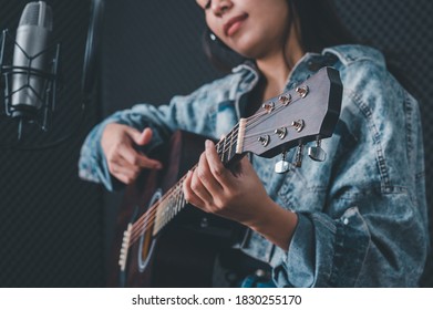Asian female singer with a passion for music and microphone. While playing her guitar in a professional studio. Music concept, sound recording concept.
