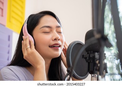 An Asian Female Singer Wearing And Holding Headphones While Singing