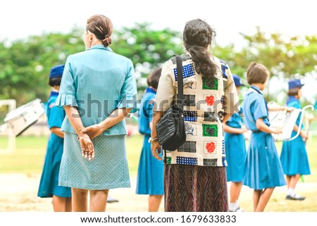 Asian female teacher stand to control the students playing music while lining up to pay respect to the national flag in the morning in school.