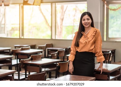 The Asian Female Teacher Is  Standing In The Empty Classroom.