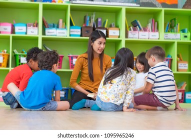 Asian female teacher teaching mixed race diversity group of kids reading book sitting on library floor in classroom,Kindergarten pre school concept - Powered by Shutterstock