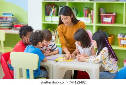 Asian female teacher teaching mixed race kids reading book in classroom,Kindergarten pre school concept