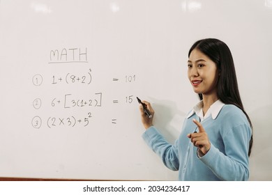 Asian Female Teacher Is Teaching Students At The Classroom While Pointing At Numbers On The White Board.