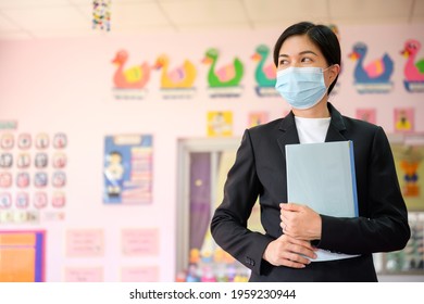 Asian female teacher wearing mask to prevent spread of COVID 19 in classroom without students while waiting for the school to reopen