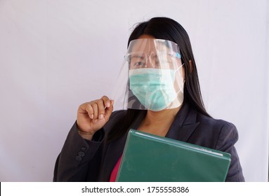 Asian Female Teacher Wearing Protective Facemask And Face Shield , Holding Green Folder Before Going Out To Teach. New Nornal Lifestyle In Covid-19  Ages.