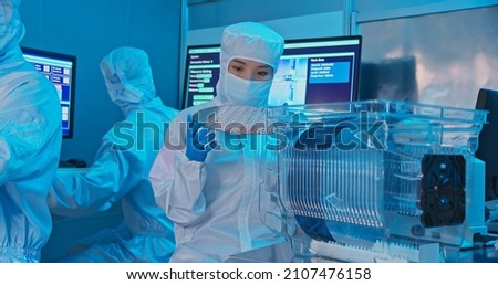 asian female technician in clean room suit holds wafer that reflects many different colors with gloves and check it at semiconductor manufacturing plant