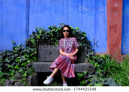 An Asian female tourist in a bright pink African pattern dress sitting on a stone garden bench