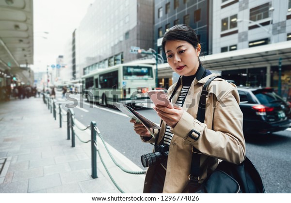 asian female tourist using online city guide on\
smartphone gps in urban street searching locations. young girl\
traveler self guided travel trip in kyoto japan standing on busy\
street holding map.