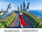 Asian female tourist walks on golden bridge in Ba Na hills, Danang, Vietnam