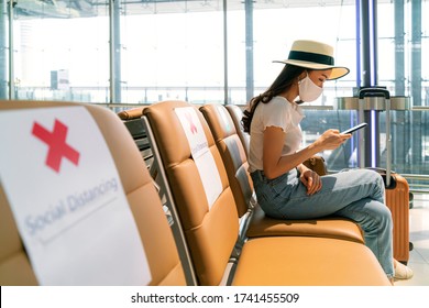 Asian female tourist wearing mask using mobile phone searching airline flight status and sit social distancing chair in airport during coronavirus or covid-19 virus outbreak a new normal concept - Shutterstock ID 1741455509