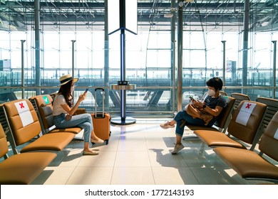 Asian female tourist wearing mask using mobile phone searching airline flight status and sit social distancing chair in airport during coronavirus or covid-19 virus outbreak a new normal concept
