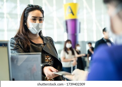 Asian female traveler giving passport to customer check in officer at airline service counter. Woman wearing face mask when traveling by airplane transportation to prevent covid19 virus pandemic.