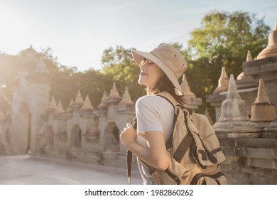 Asian female traveler smile wearing a hat with backpack in the attraction Asia culture under sunshine. Travel Southeast Asia culture. Pagoda of Buddhist in Thailand.