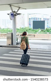 Asian Female Traveller Crossing The Road With Her Rolling Suitcase At The Airport. 