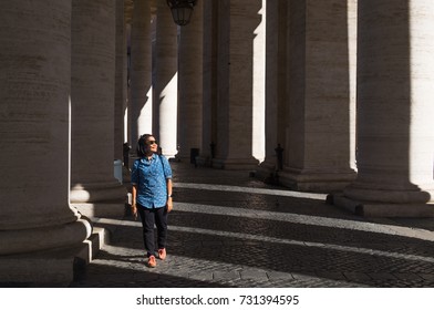 An Asian Female Traveller In Denim Costume Walking Through Lines Of Old Pillars That Having Light And Shadow Pattern. Model Is Not Looking At Camera.