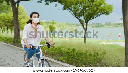 Asian female wear mask with smile and ride bicycle in the park