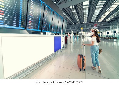 Asian female wearing face mask with suitcase checking flight cancellation status on airport information board in empty airport. airline bankrupt, airline crisis, coronavirus or new normal concept