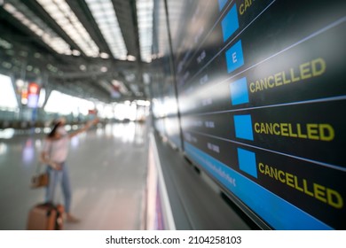 Asian female wearing face mask with suitcase checking flight cancellation status on airport information board in empty airport. airline bankrupt, airline crisis or new normal concept