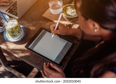 Asian Female Worker Uses Her Tablet And Pen Sitting At Table Outside