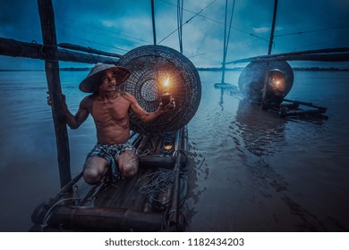 Asian Fisherman Holding A Lantern On His Boat Waiting To Fish In The Mekong. During The Twilight