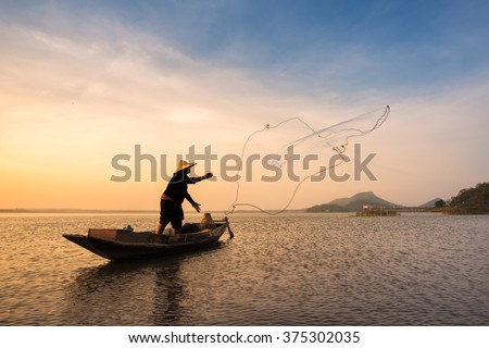 Asian fisherman on wooden boat casting a net for catching freshwater fish in nature river.