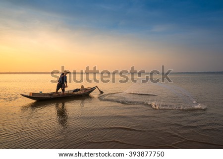 Asian fisherman on wooden boat throwing a net for catching freshwater fish in nature river in the early morning before sunrise