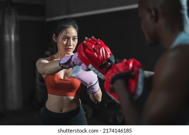 Asian fit female boxing training with her trainer at gym.Sportwoman  wearing boxing gloves exercise and punch to pads for boxing