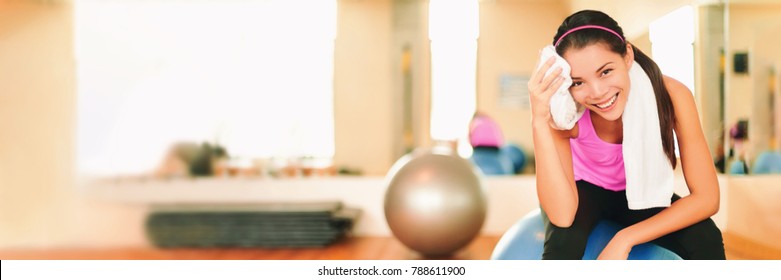 Asian Fitness Girl Training At Gym Wiping Sweat With Towel Post Workout Happy In Gym Background. Panorama Crop With Copy Space On Gym Interior. Exercise And Healthy Living Weight Loss Concept.