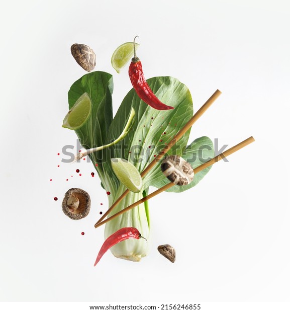 Asian food concept with flying ingredients:
Bok choy , chopsticks, lime, shiitake, spices and chili  at white
background. Levitation  food. Front
view.