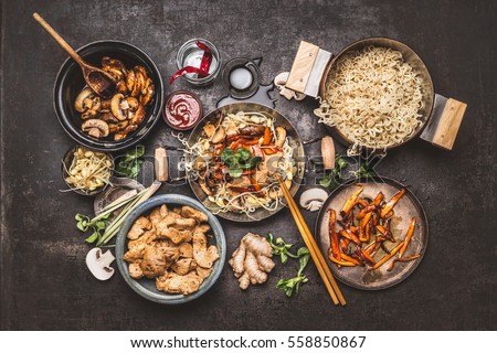 Asian food cooking. Wok with noodles chicken stir fry and vegetables ingredients with spices ,sauces and chopsticks on dark rustic background, top view