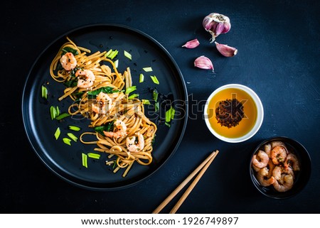 Asian food - noodles with prawns in soy sauce with spinach on black table