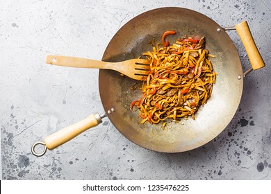 Asian food, stir fry udon noodles with meat and vegetables in a wok pan on gray stone background, top view