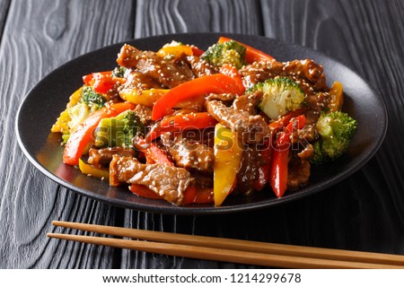 Asian food: teriyaki beef with red and yellow bell peppers, broccoli and sesame seeds close-up on a plate on a black table. horizontal
