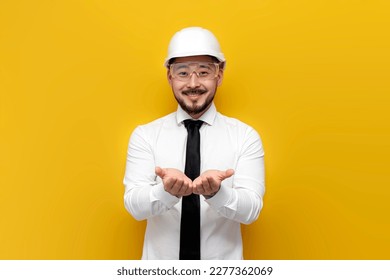 asian foreman in shirt with tie holds blank space with his hands on yellow isolated background, korean civil engineer in formal wear holds his hands in front of him - Shutterstock ID 2277362069