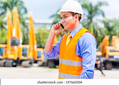 Asian foreman telephoning with mobile phone of building site or mining or rental company