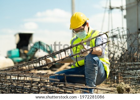 asian foreman wearing protective face mask checking steel structure outdoors on construction site. contractor worker Inspection and correction rebar steel cage . quality control of industry