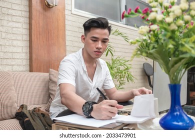 An asian freelance assistant or university student writes down some notes on a piece of paper. Working at home.