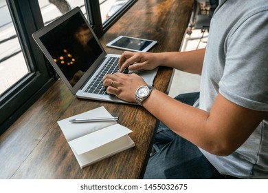 Asian freelancer using laptop at rustic coffee table near window
