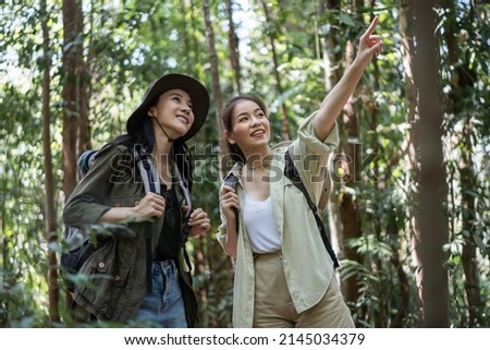 Asian friend girls backpacker friend travel in forest wild together. Attractive young women couple traveler walk and exploring nature wood with happiness and fun during holiday vacation trip on summer