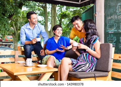 Asian Friends Or Colleagues Enjoying Leisure Time In A Cafe, Drinking Coffee Or Cappuccino And Looking At Photos Or Emails On A Tablet Computer