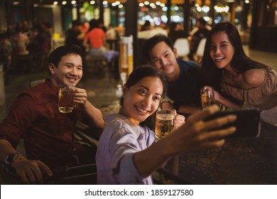 Asian Friends Drinking Beer Outdoors At The Brewery For The New Year Festival.She Is Taking A Selfie Night Time