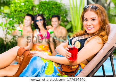 Asian friends partying and drinking fancy cocktails at hotel or club pool party