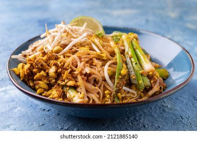 Asian fusion vegan meat-free meal with noodles, sprout, spring onion and fried spicy peanuts on blue background