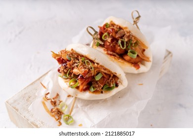 Asian fusion vegan white soft bao with fermented and fresh vegetables, spicy sauce and crunchy onion flakes on white