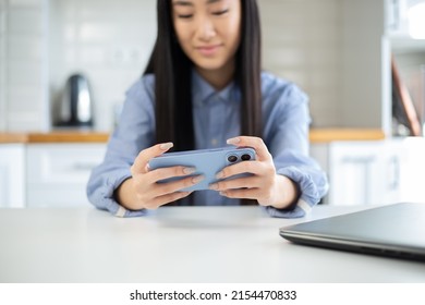 Asian Gamer Girl Playing Mobile Games On Modern Smartphone. Happy Vietnamese Female Plays Video Game App On Mobile Phone In Free Time