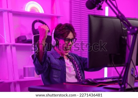 Asian gamer with a happy expression and raised fists in front of a computer screen,Celebrating winning a online video game. Professional gamer concept