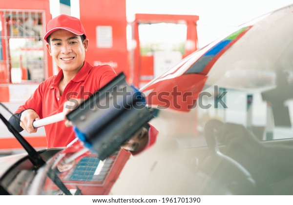 Asian gas station worker man cleaning\
windshield while car owner waiting for filling high energy power\
fuel in car tank into petrol station, commercial service for\
benzine, diesel, gasohol,\
gasoliine