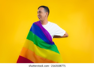 Asian Gay Man With A Gay Pride Flag Smiling And Looking Away On Yellow Background.
